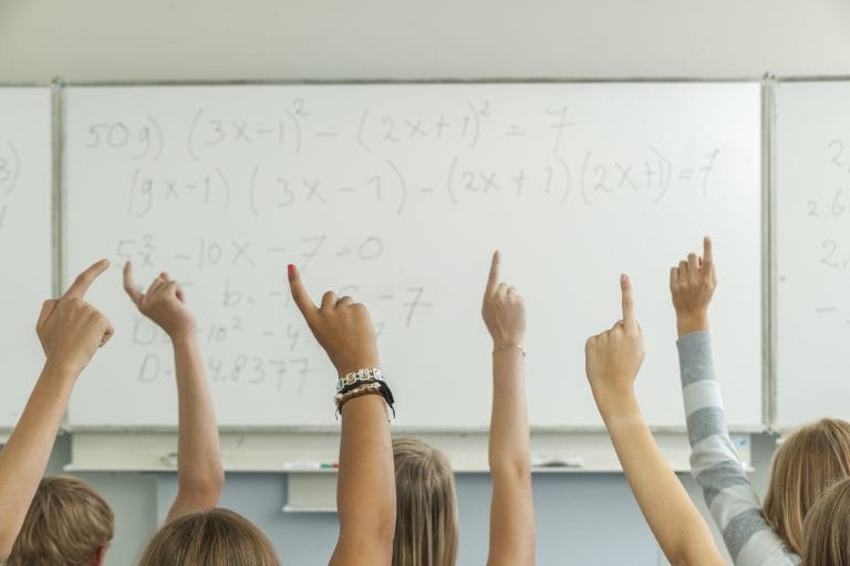 High school students in classroom raising hands